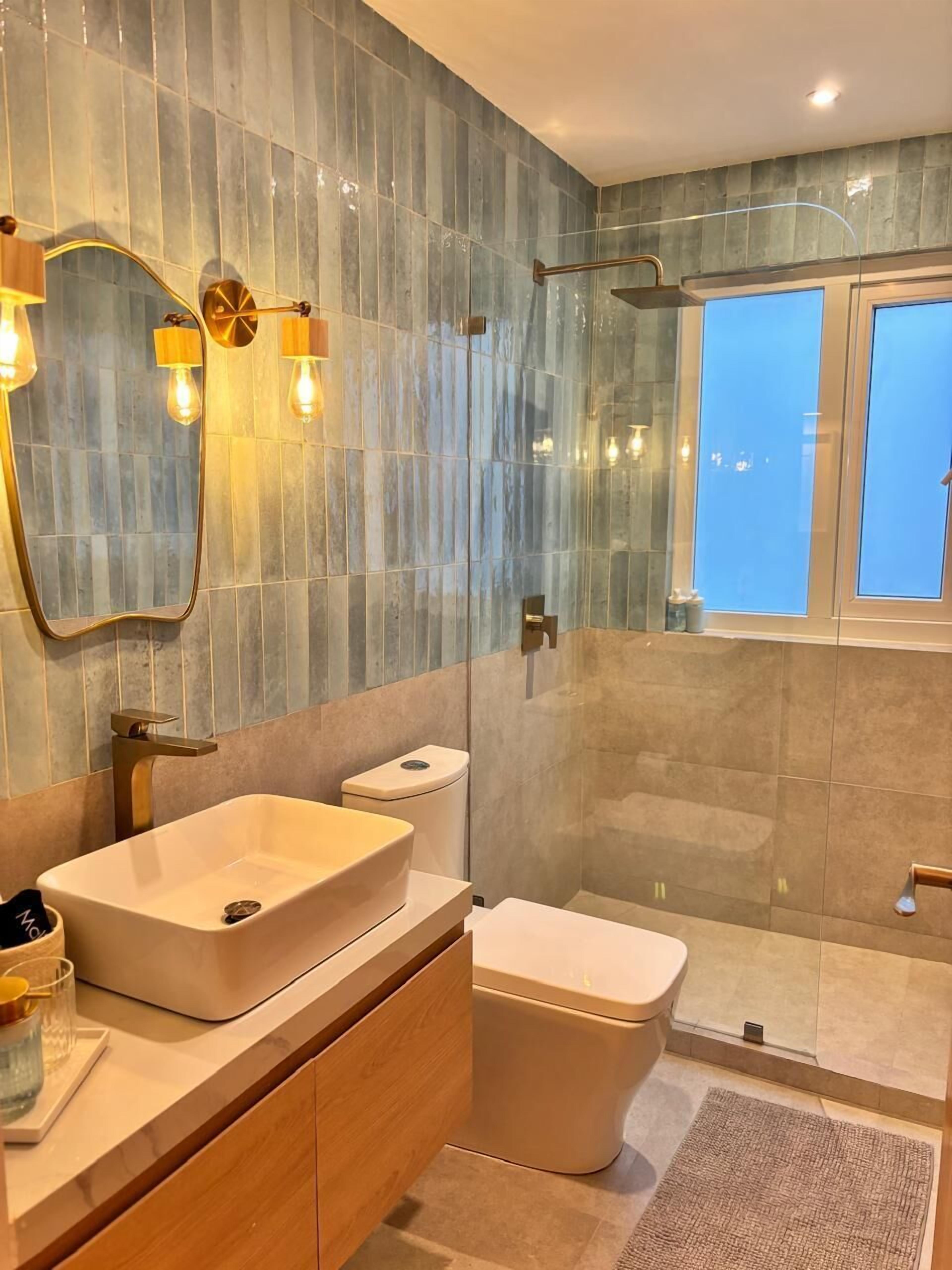 Un baño moderno con un espejo grande, un lavamanos sobre encimera, un inodoro y una zona de ducha.