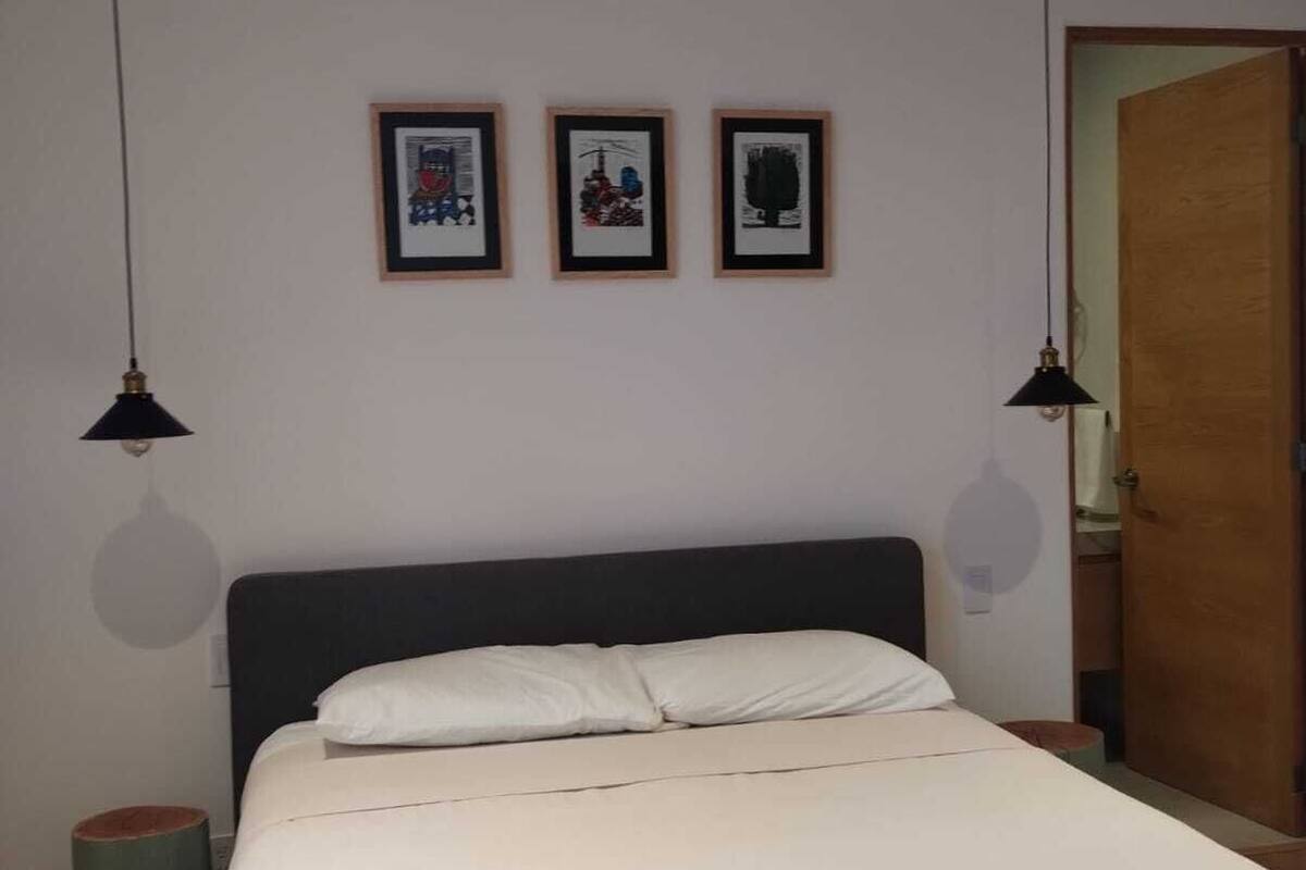 A neatly made bed with two white towels, a dark headboard, and three framed artworks on the wall.
