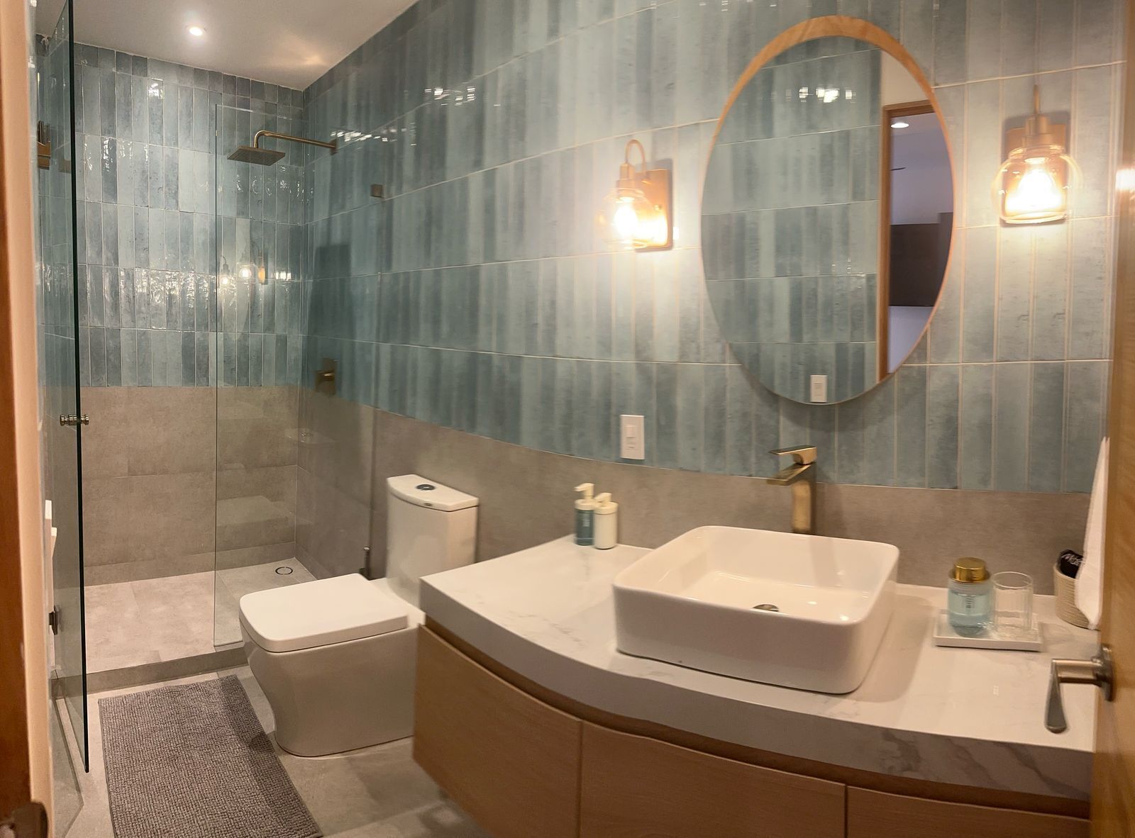 A modern bathroom with a glass-enclosed shower, a white sink with a gold faucet, and a large mirror.