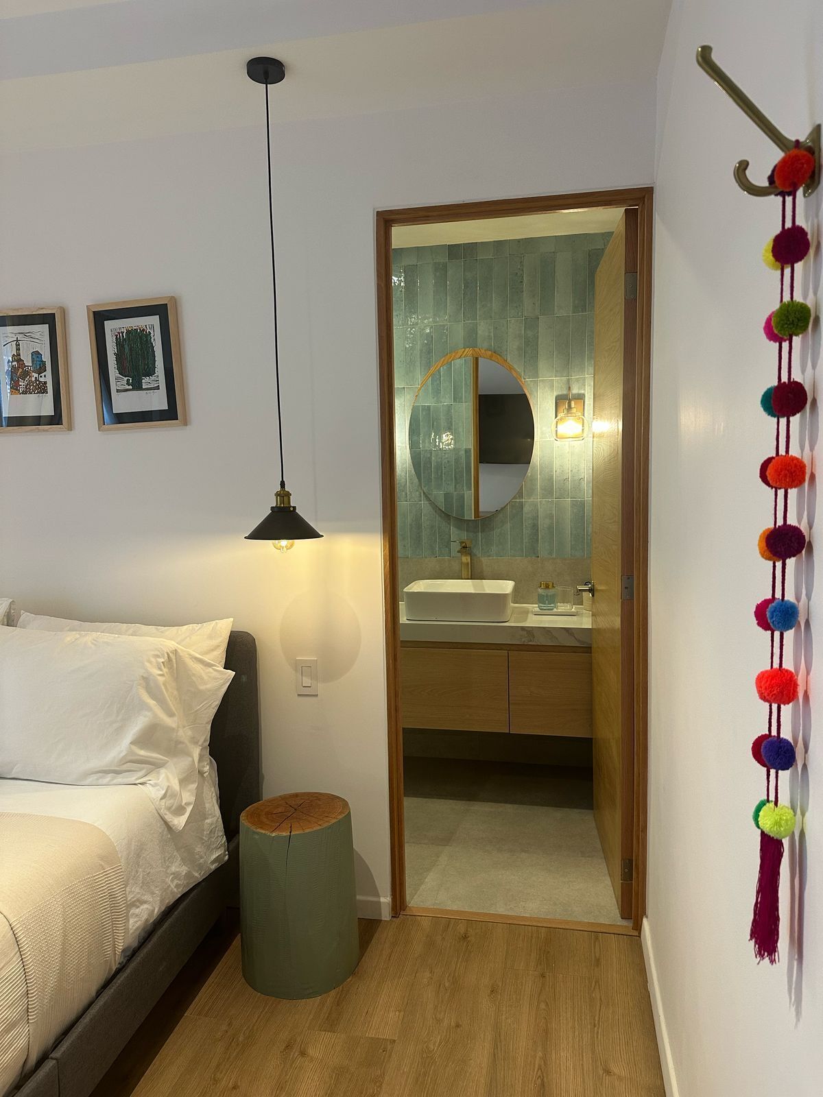 A bedroom with a bed, a bedside lamp, a round mirror, and a small round table.