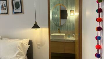 A bedroom with a bed, a bedside lamp, a round mirror, and a small round table.
