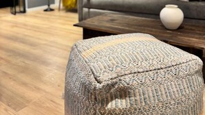 Een moderne woonkamer met een grijze bank, een bijzettafeltje en een gestreept voetenbankje.