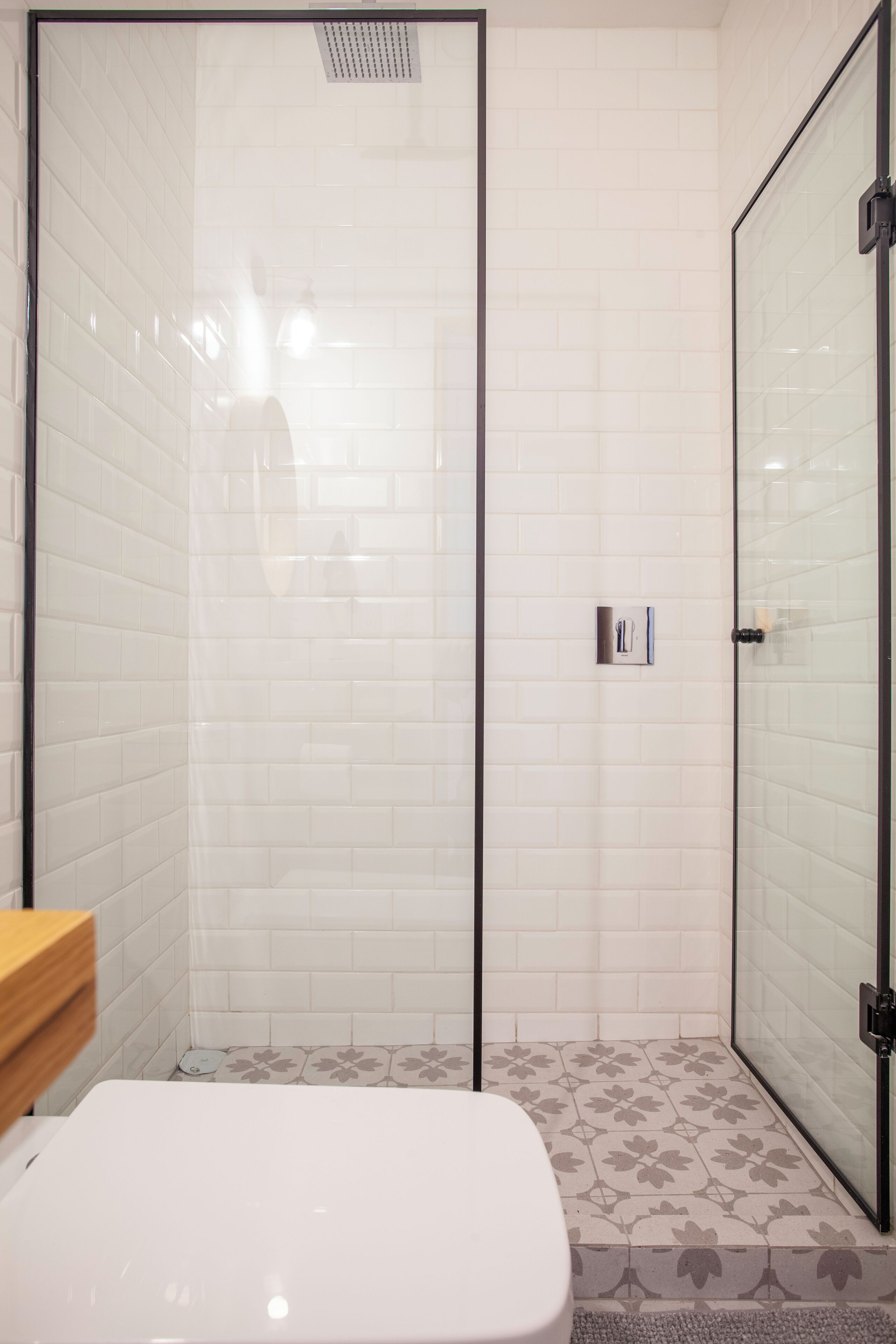 Un baño con inodoro blanco, cabina de ducha de vidrio y suelo estampado.