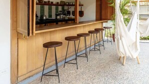 A wooden bar area with stools, a hammock, and a kitchen with shelves and utensils. - Casa Cadejo- Surf paradise in Playa Grande (Playa Grande)