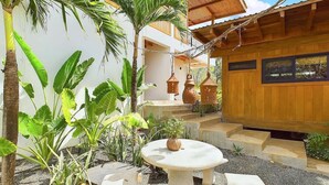 A courtyard with a wooden building, a stone table with a plant, and tropical plants. - Casa Cadejo- Surf paradise in Playa Grande (Playa Grande)
