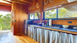 A kitchen with wooden walls, a window with a view of greenery, and a counter with kitchen utensils. - Casa Cadejo- Surf paradise in Playa Grande (Playa Grande)
