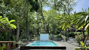 A rectangular swimming pool with a white deck in the center, surrounded by gravel and steps leading to it. - Casa Cadejo- Surf paradise in Playa Grande (Playa Grande)