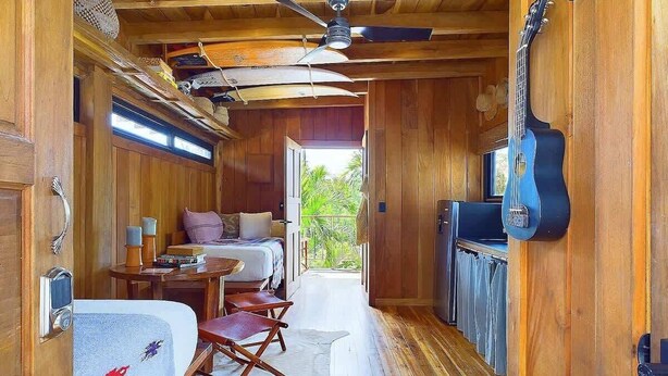 A compact, wood-paneled room with a bed, a small table, and a guitar. - Casa Cadejo- Surf paradise in Playa Grande (Playa Grande)