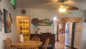 A dining area with a wooden table and chairs, a ceiling fan, and a kitchen with a refrigerator and cabinets. - Charming 2-bedroom house with WiFi, AC in welcoming Port Lavaca (Port Lavaca)