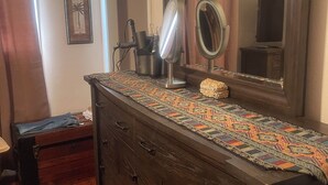 A wooden dresser with a mirror and a patterned cloth, a small table with a lamp, and a window with curtains. - Charming 2-bedroom house with WiFi, AC in welcoming Port Lavaca (Port Lavaca)