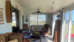 A spacious living area with a ceiling fan, a large window with blinds, a leather sofa, a wooden coffee table, and a view of the outdoors. - Charming 2-bedroom house with WiFi, AC in welcoming Port Lavaca (Port Lavaca)