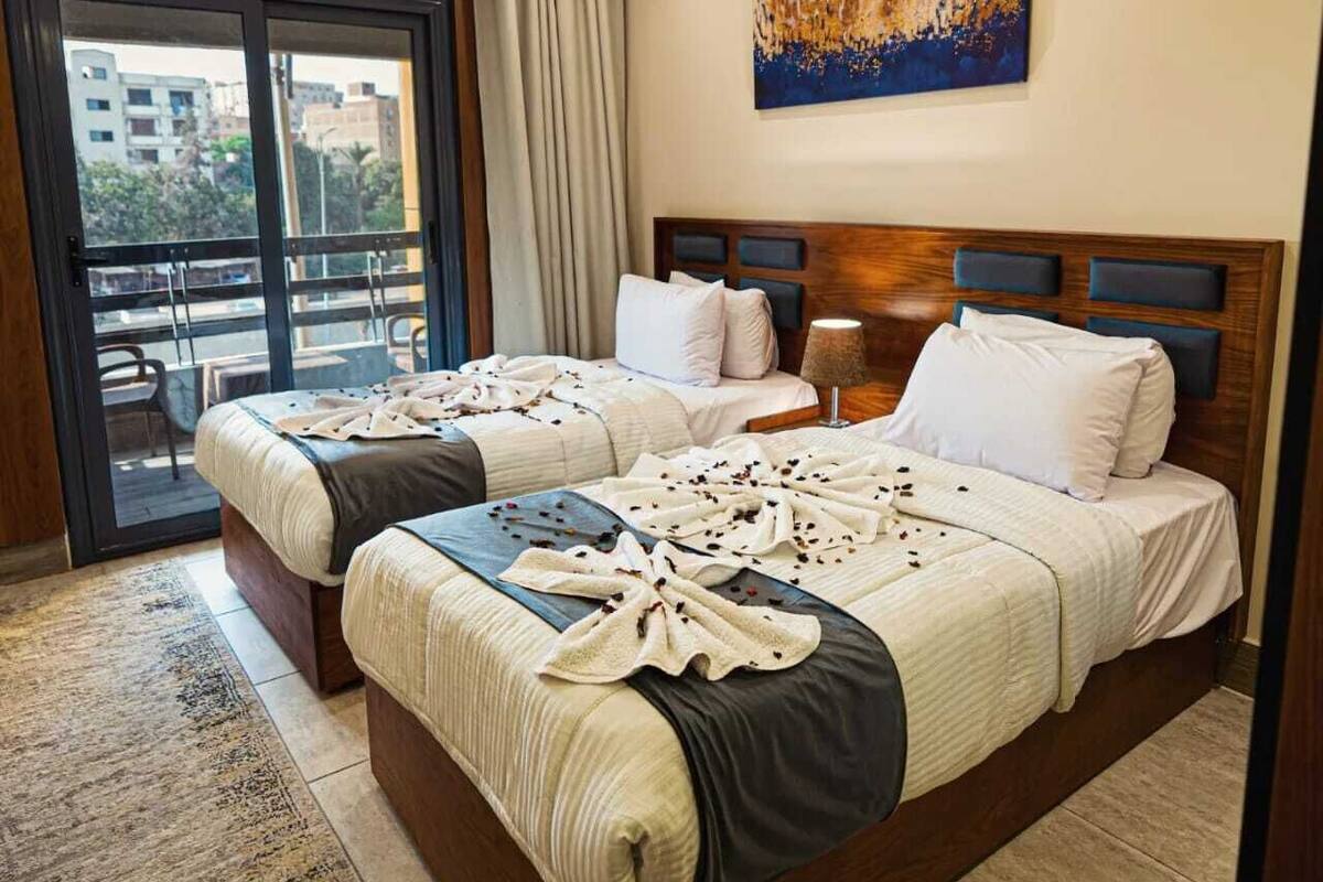 A hotel room with two beds, a balcony, and a city view.