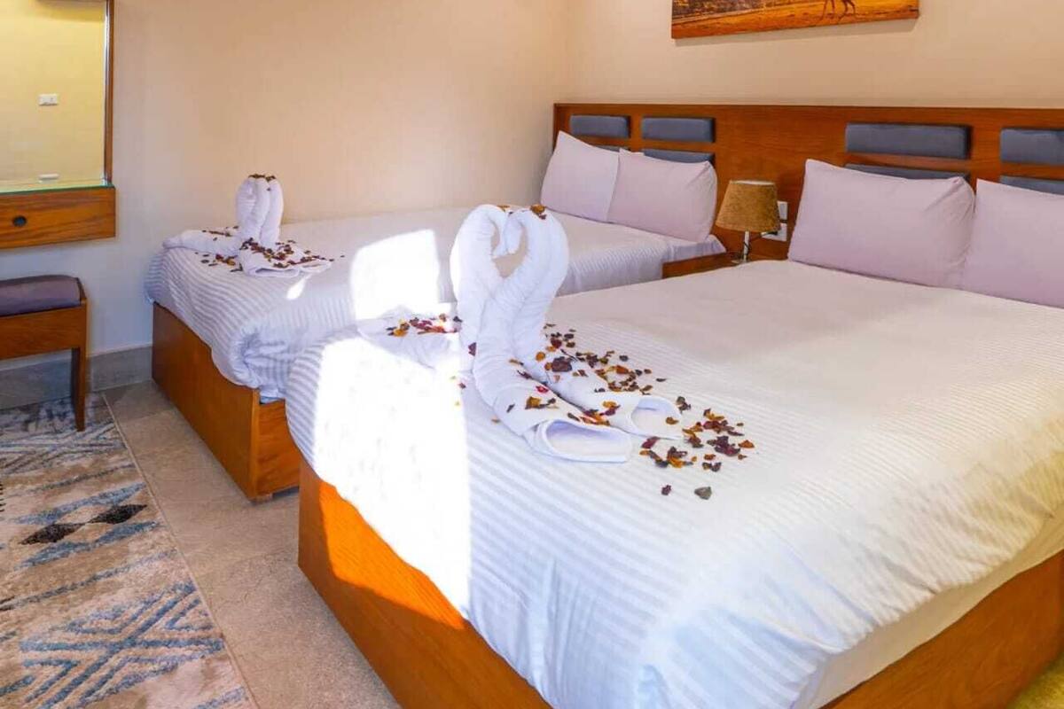 A hotel room with two beds, a wooden headboard, a painting of a desert landscape, and a mirror on the wall.