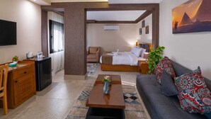 A hotel room with a bed, a sofa, a desk, and a TV. - Zahira pyramids view (Giza)