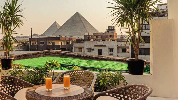 A balcony with wicker furniture, two drinks, and a view of the pyramids. - Zahira pyramids view (Giza)