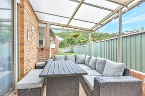 A covered outdoor seating area with a built-in bench and table, surrounded by a brick wall and a metal fence.