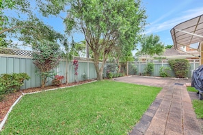 A backyard with a grassy lawn, a tree, and a covered patio area.