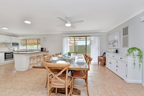 A modern kitchen with white cabinetry, a dining area with wooden chairs, and a large window with curtains.