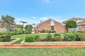 A residential house with a brick exterior, a well-maintained lawn, and various shrubs. - The Fingal Escape (Fingal Bay)