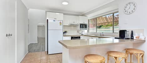 A modern kitchen with white cabinets, a central island with stools, a microwave, and a clock on the wall.