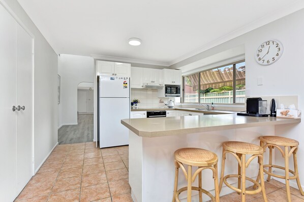 A modern kitchen with white cabinets, a central island with stools, a microwave, and a clock on the wall.