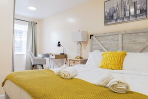 A hotel room with a bed, a desk, a chair, a lamp, and a cityscape painting on the wall. - Spacious 3BR Oasis w/ Patio & Arcade Fun in Philly (Philadelphia)