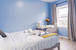 Une chambre à coucher avec un lit, un bureau, une chaise et une fenêtre avec des rideaux.