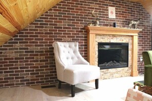 A room with a brick fireplace, a white upholstered armchair, and a green chair. - Spacious 3BR Oasis w/ Patio & Arcade Fun in Philly (Philadelphia)
