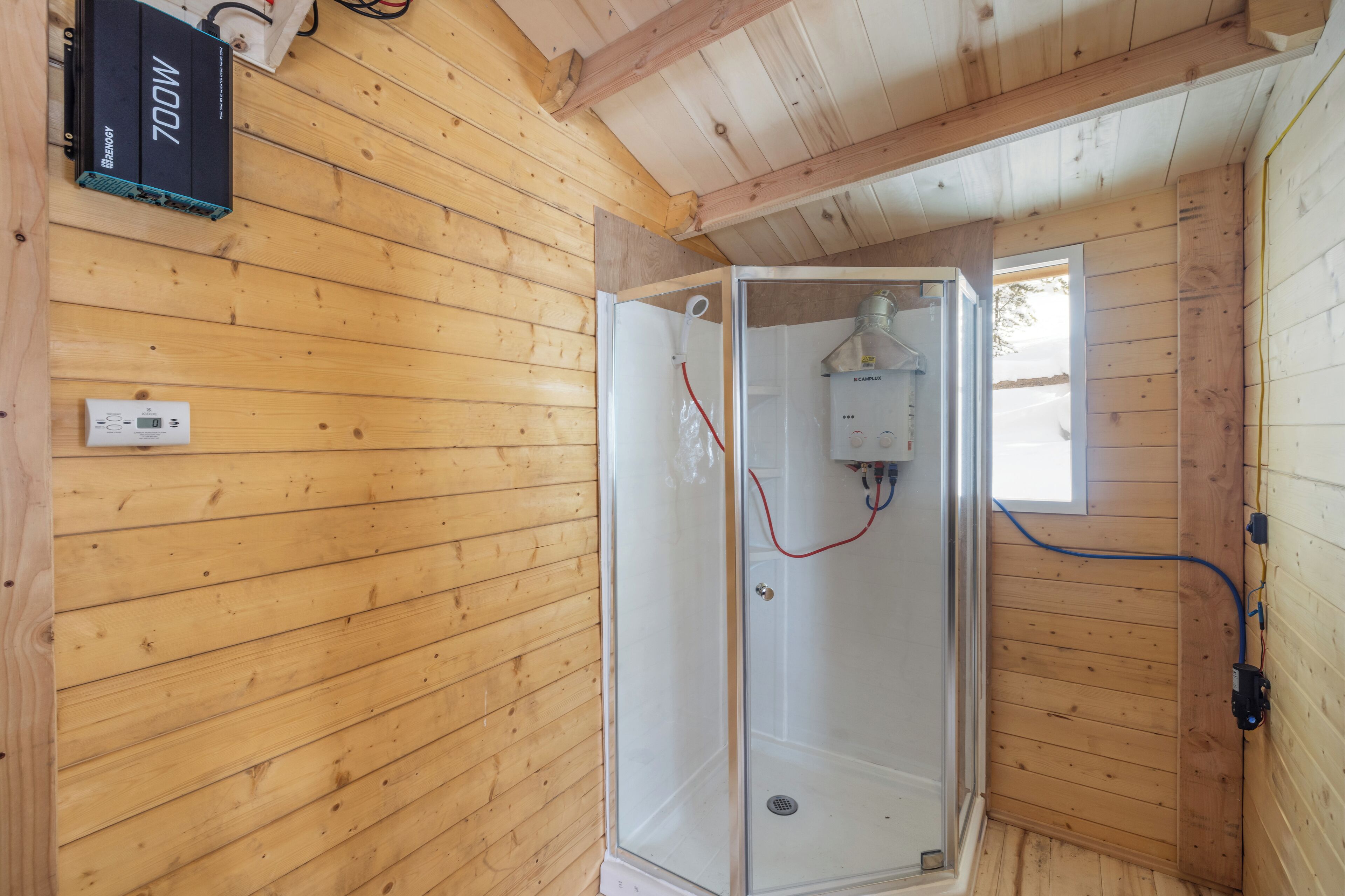 A wooden cabin interior with a glass-enclosed shower, a power outlet, and a window.