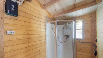 A wooden cabin interior with a glass-enclosed shower, a power outlet, and a window.