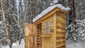 A wooden cabin with a door open, surrounded by snow-covered trees.