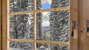 A room with a large window offering a view of snow-covered trees and mountains.