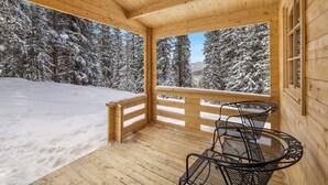 A wooden cabin with a balcony overlooking a snowy forest.