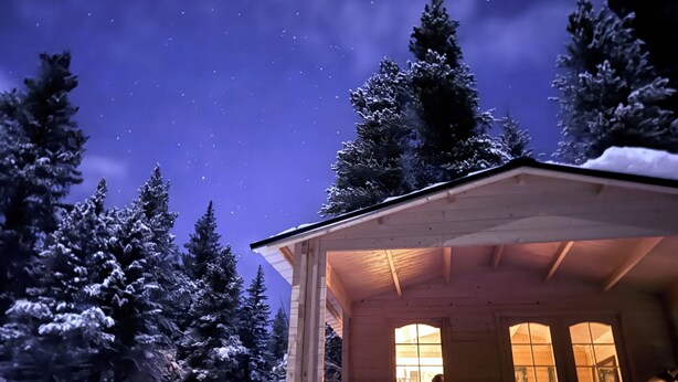 A wooden cabin with a porch, surrounded by snow-covered trees, under a starry night sky.
