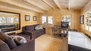 A wooden cabin interior with a sofa, a dining table, and a kitchen area with a stove.
