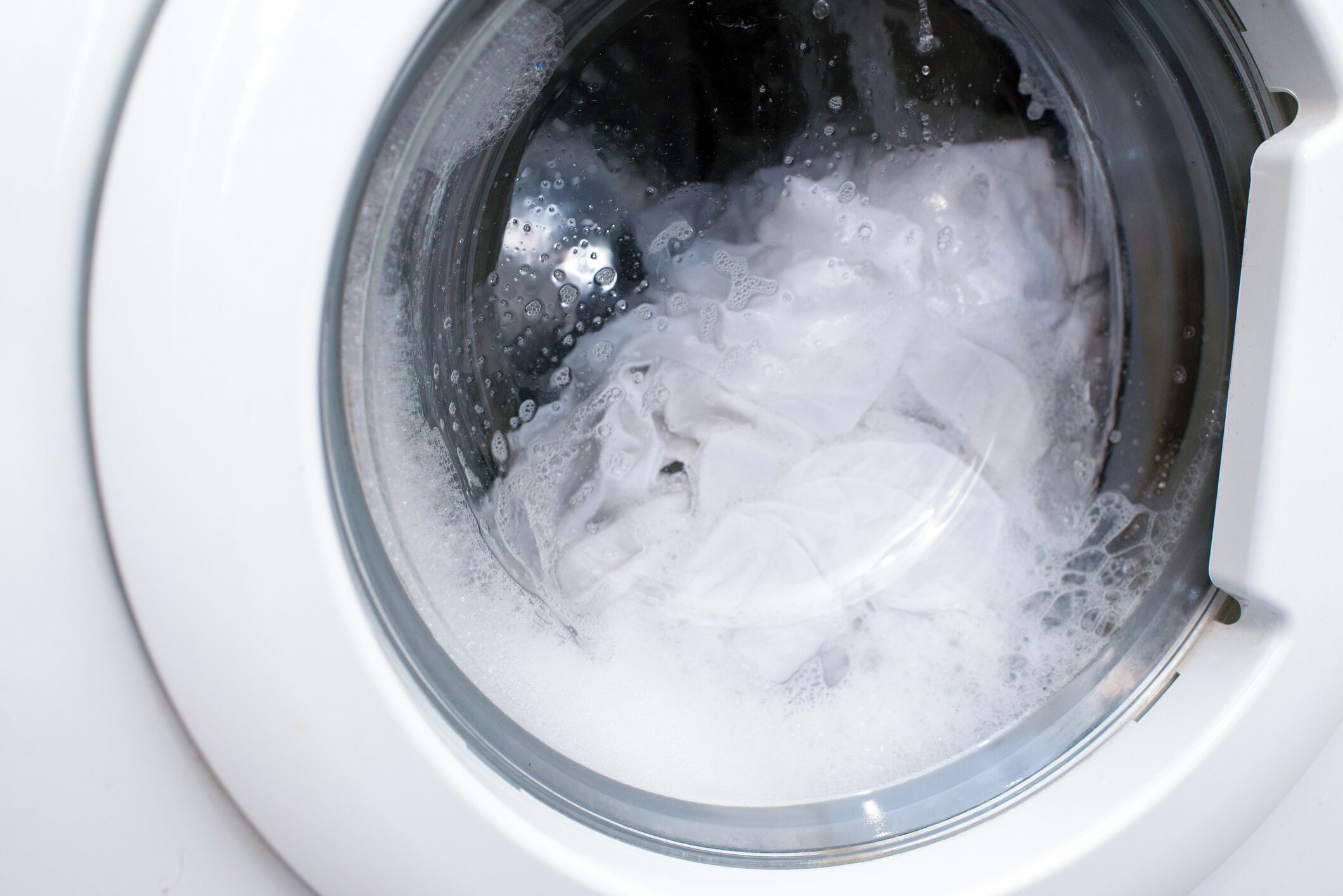A washing machine in operation with water and foam inside.