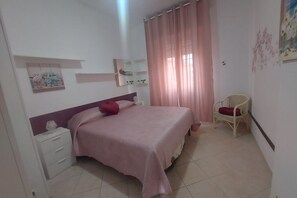 A bedroom with a bed, a nightstand, a chair, and a window with curtains. - "The Hawthorn Pitchers" Apartments (Tor San Lorenzo)