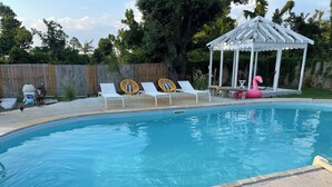 En swimmingpool med solstolar och en lusthus.