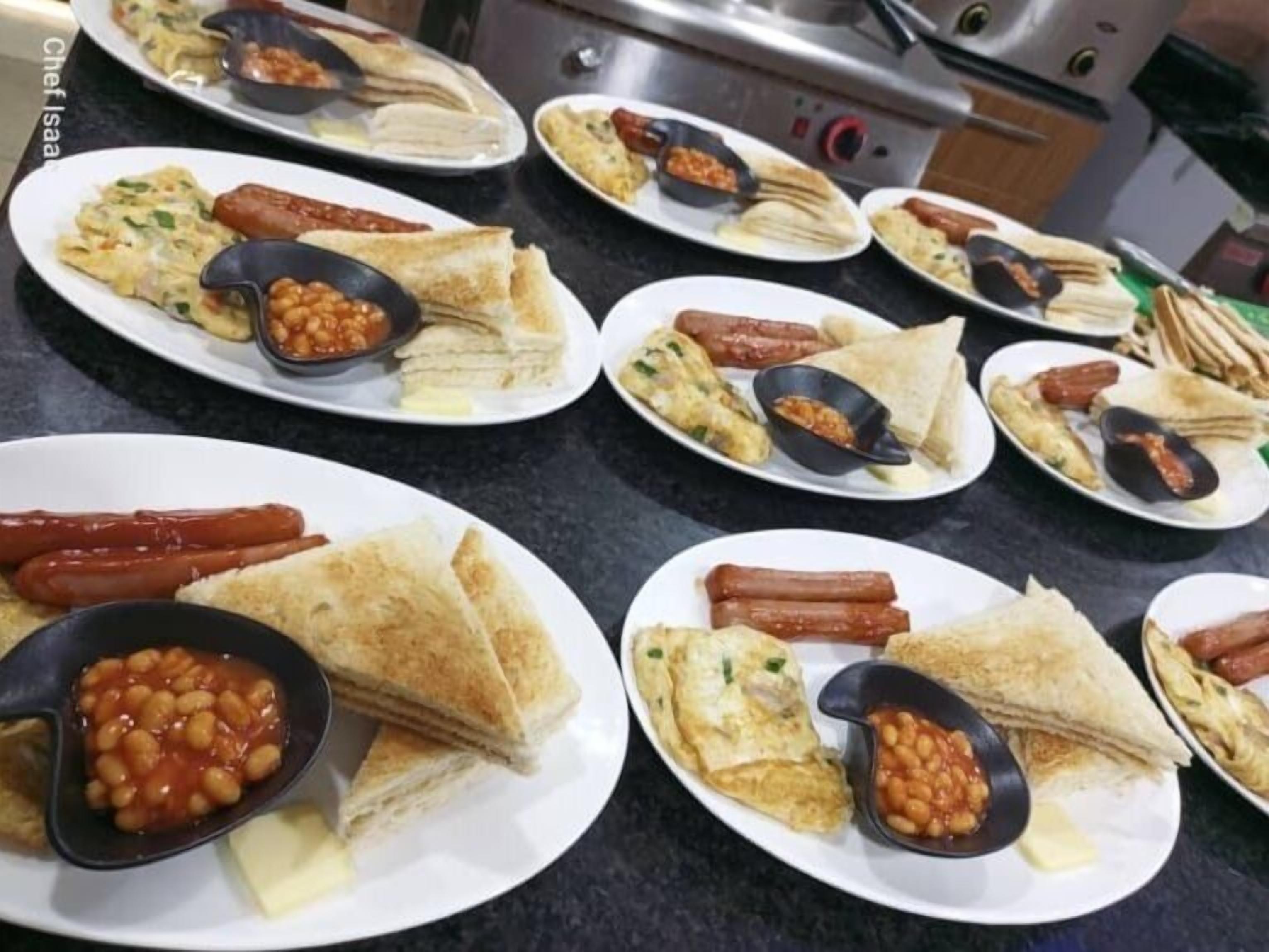 A kitchen counter with multiple plates of food, including sandwiches, hot dogs, and beans.