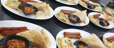 A kitchen counter with multiple plates of food, including sandwiches, hot dogs, and beans.