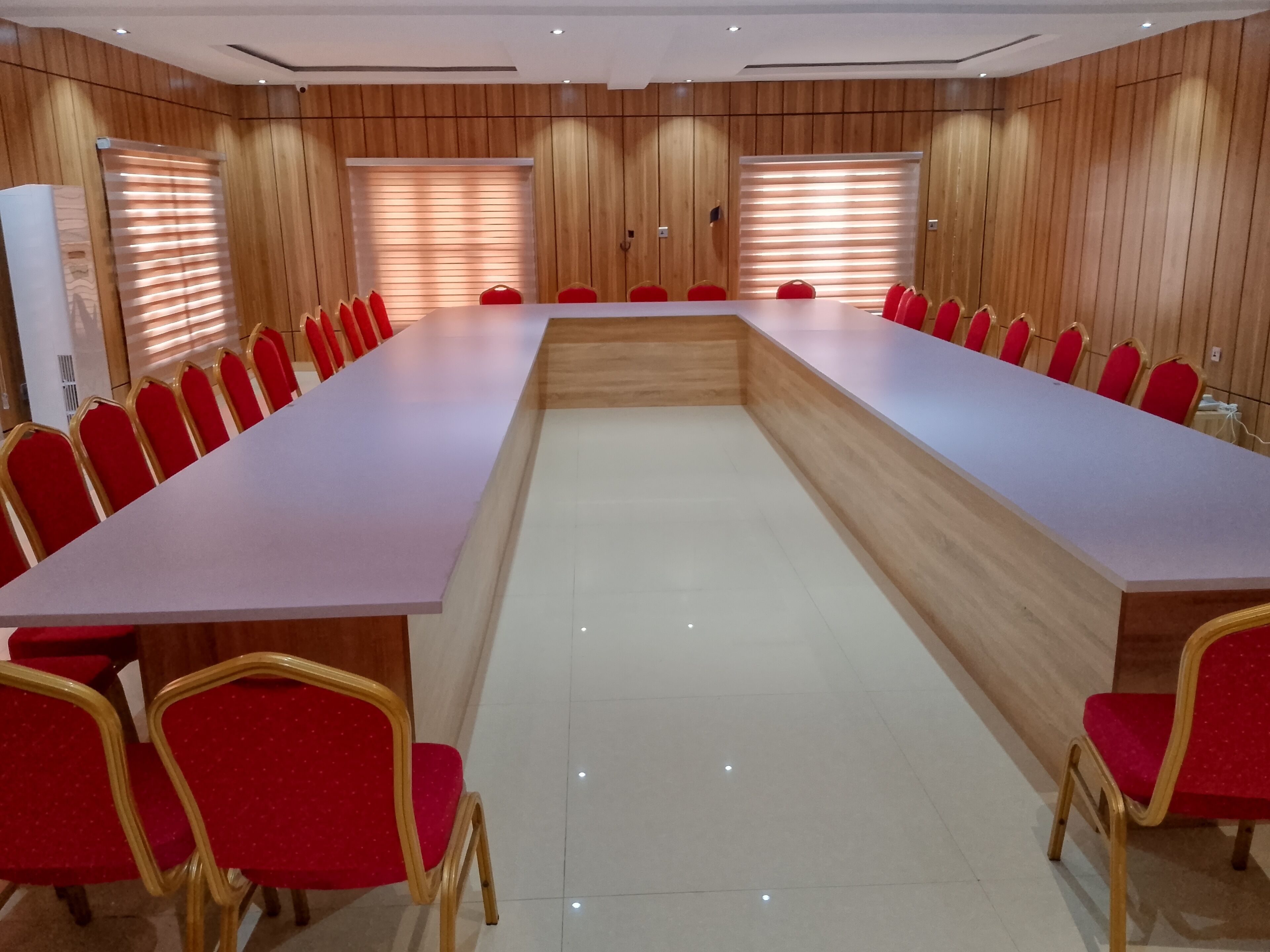 Un salón de conferencias con una larga mesa, sillas rojas y paneles de madera.