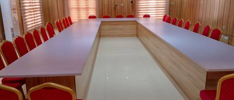Un salón de conferencias con una larga mesa, sillas rojas y paneles de madera.