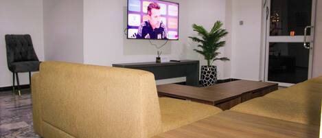 Een woonkamer met een bank, een salontafel en een flatscreen televisie die aan de muur is bevestigd.