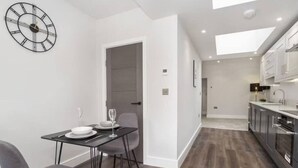 A modern kitchen with dark wood flooring, white cabinets, and a dining area with a table and chairs. - The Old Hotel - Mad Alice (Clifton)