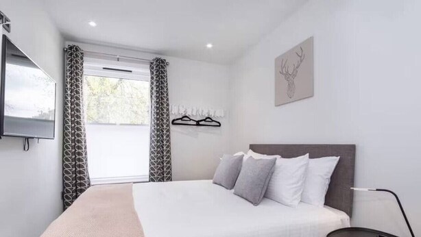 A modern bedroom with a large bed, a bedside table, and a wall-mounted TV. - The Old Hotel - Mad Alice (Clifton)