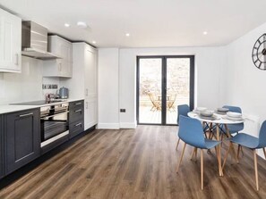 A modern kitchen with white cabinets, a built-in oven, and a dining area with blue chairs and a round table. - The Old Hotel - Three Cranes (Clifton)