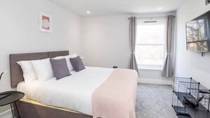 Een moderne slaapkamer met een groot bed, een klein tafeltje en een hokje voor een huisdier.
