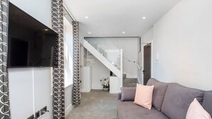 Una sala de estar moderna con un sofá gris, un televisor de pantalla plana y una escalera que sube a un segundo piso.