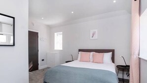 Un dormitorio moderno con una cama grande, una mesita de noche, una lámpara de pared y una ventana que deja entrar luz natural.