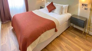 Une chambre d’hôtel moderne avec un grand lit, une table de chevet, une commode et une lampe sur pied.